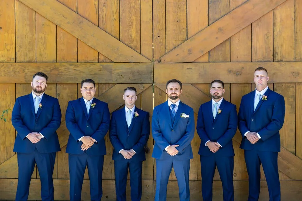 Clayton and groomsmen in navy suits in front of the Tar Creek Ranch barn