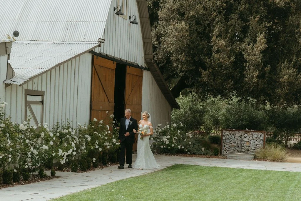 Bride entering a spring garden ceremony beside the barn at Tar Creek Ranch