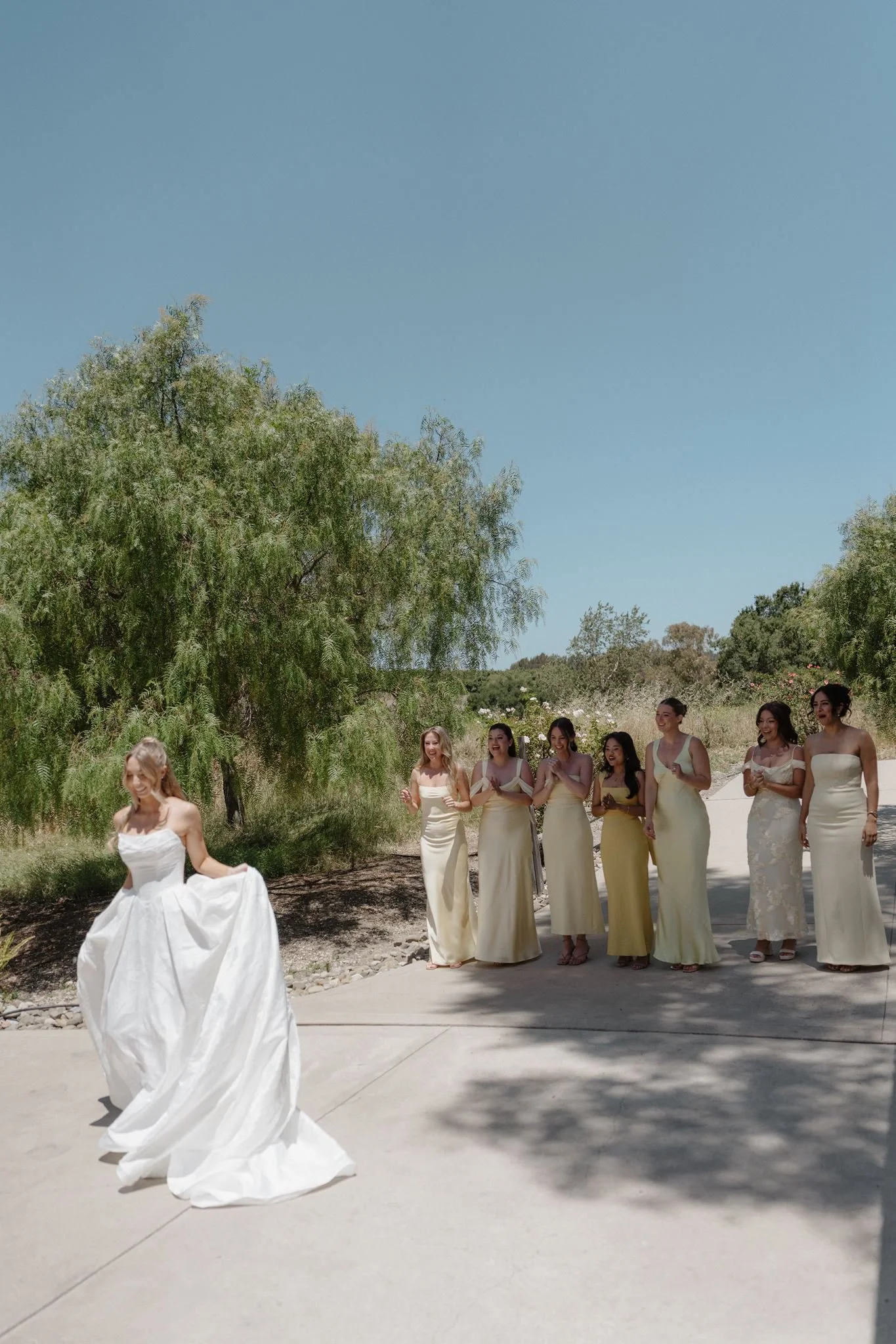 Bride twirling in front of bridesmaids in butter-yellow dresses