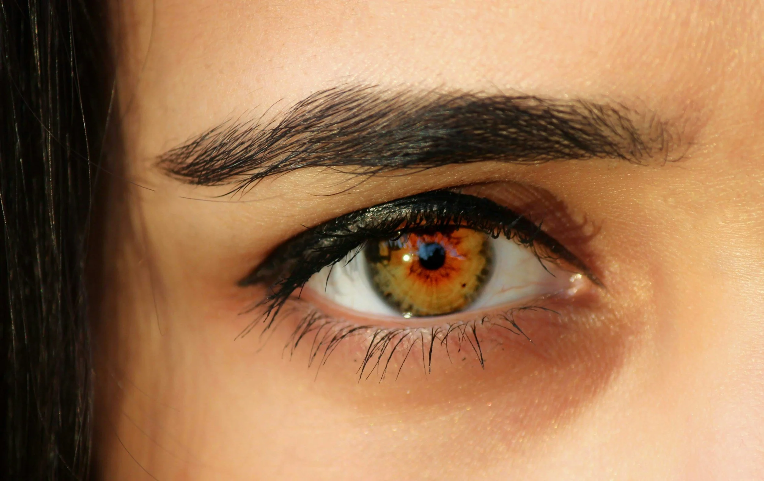 Close-up of a person's eye with brown iris and detailed eyelashes, with well-groomed eyebrows and smooth skin.