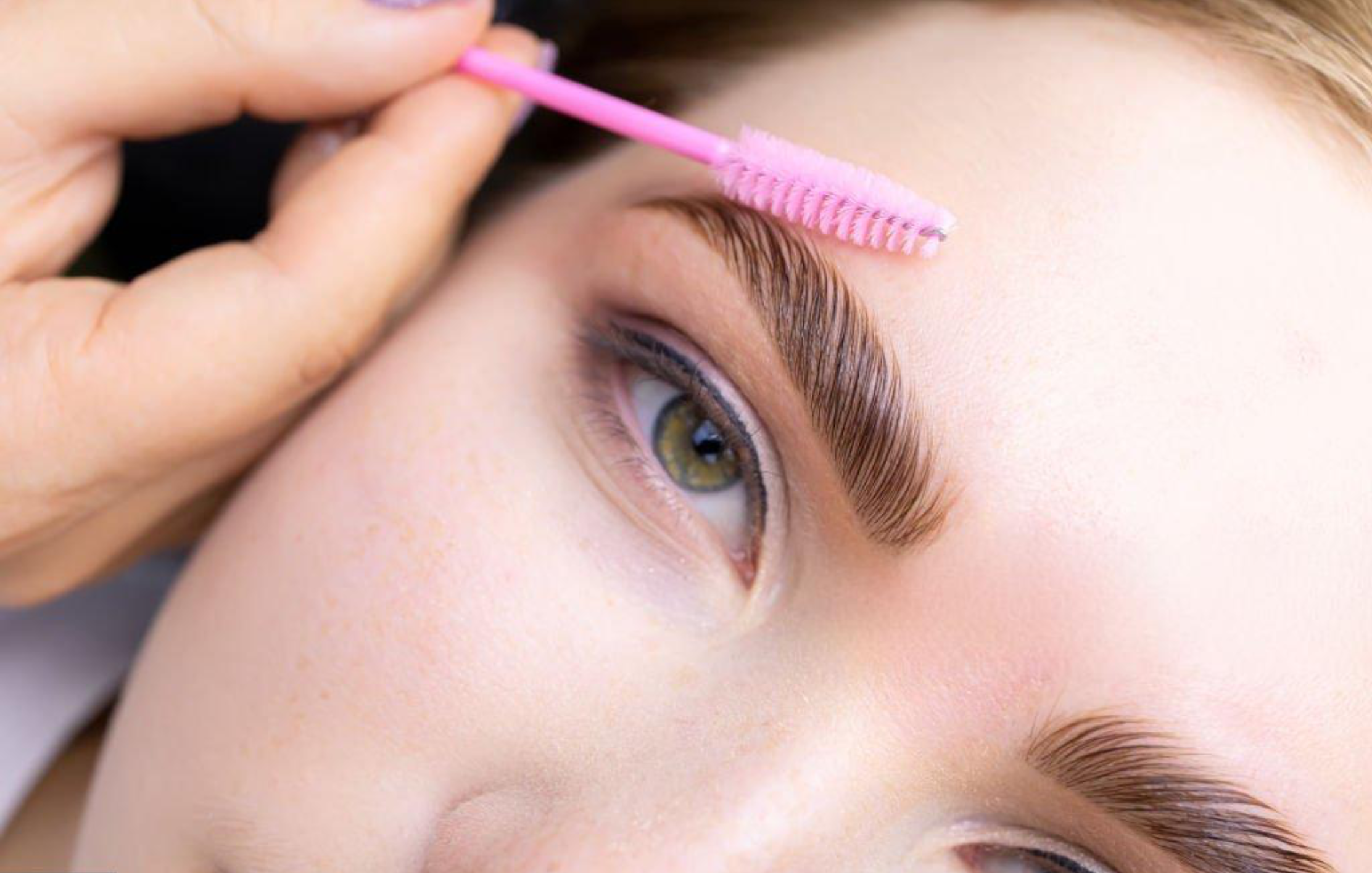 Close-up of a person cleaning eyebrows with a pink spoolie brush.