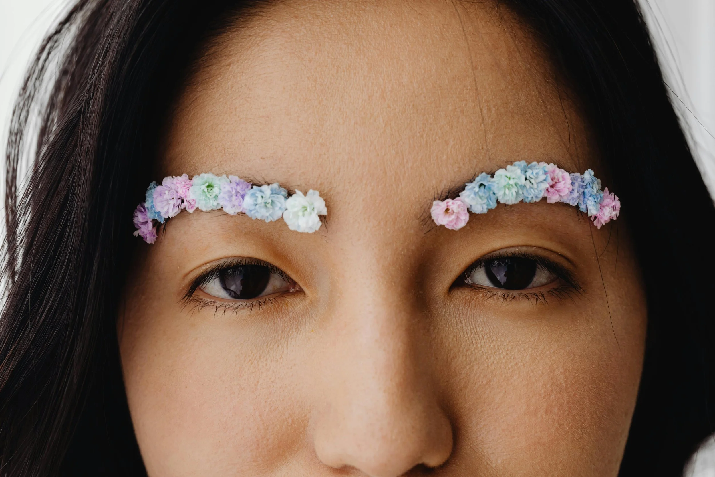 Close-up of a person's face with flowers arranged on their eyebrows.