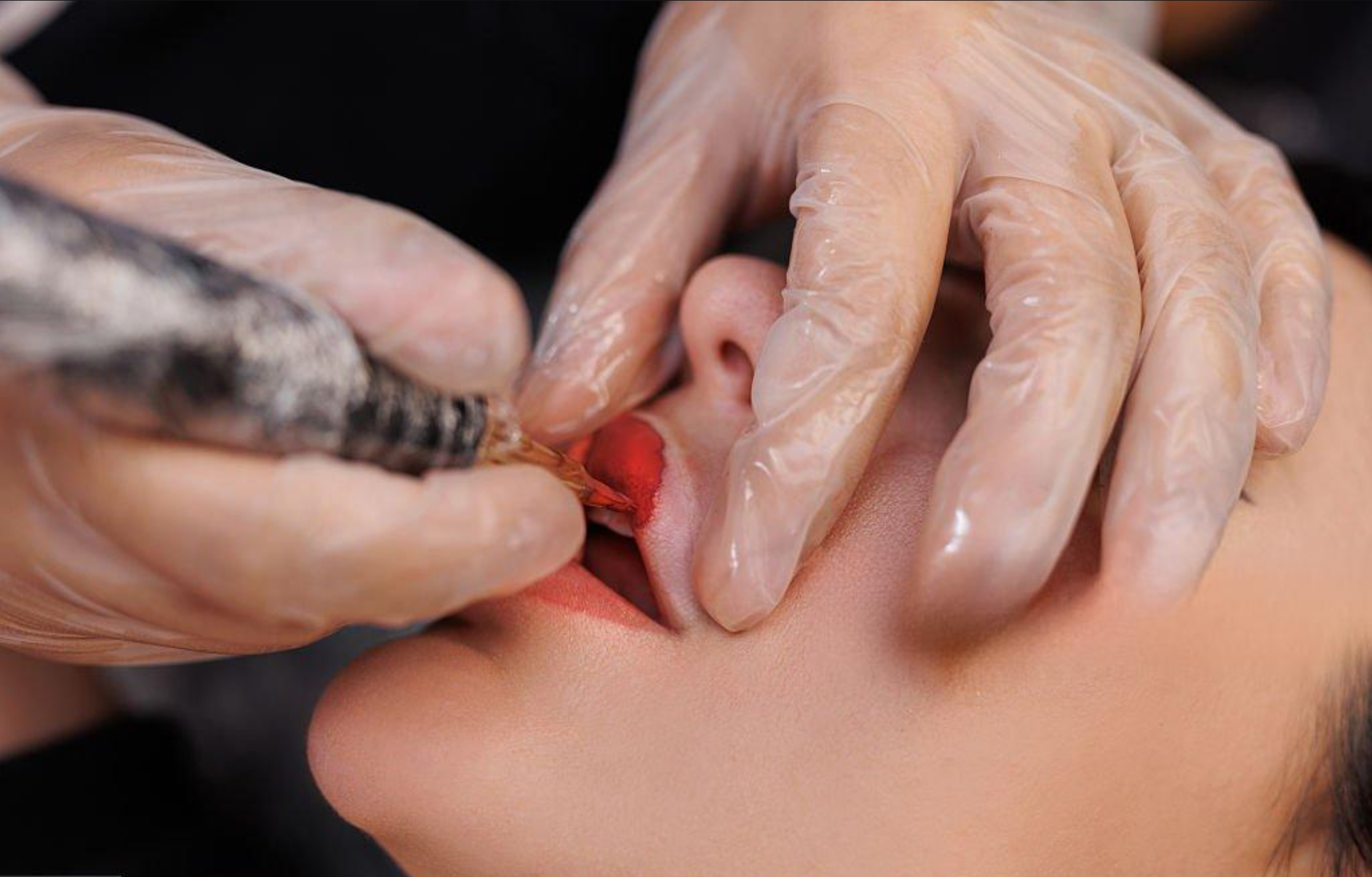 A person receiving a tattoo on their inner lip from a tattoo artist using a tattoo gun.