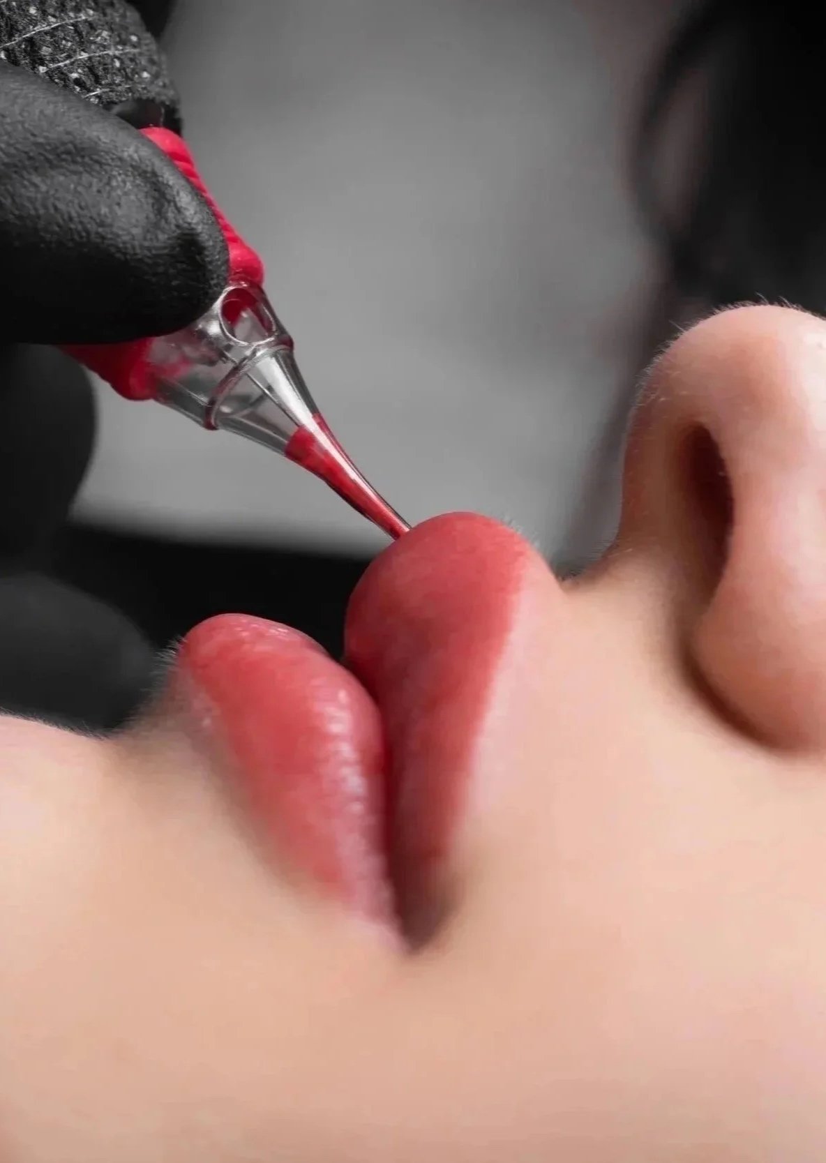 Close-up of a person receiving a nose tattoo with a tattoo needle, while another person holds the needle, all wearing black gloves.