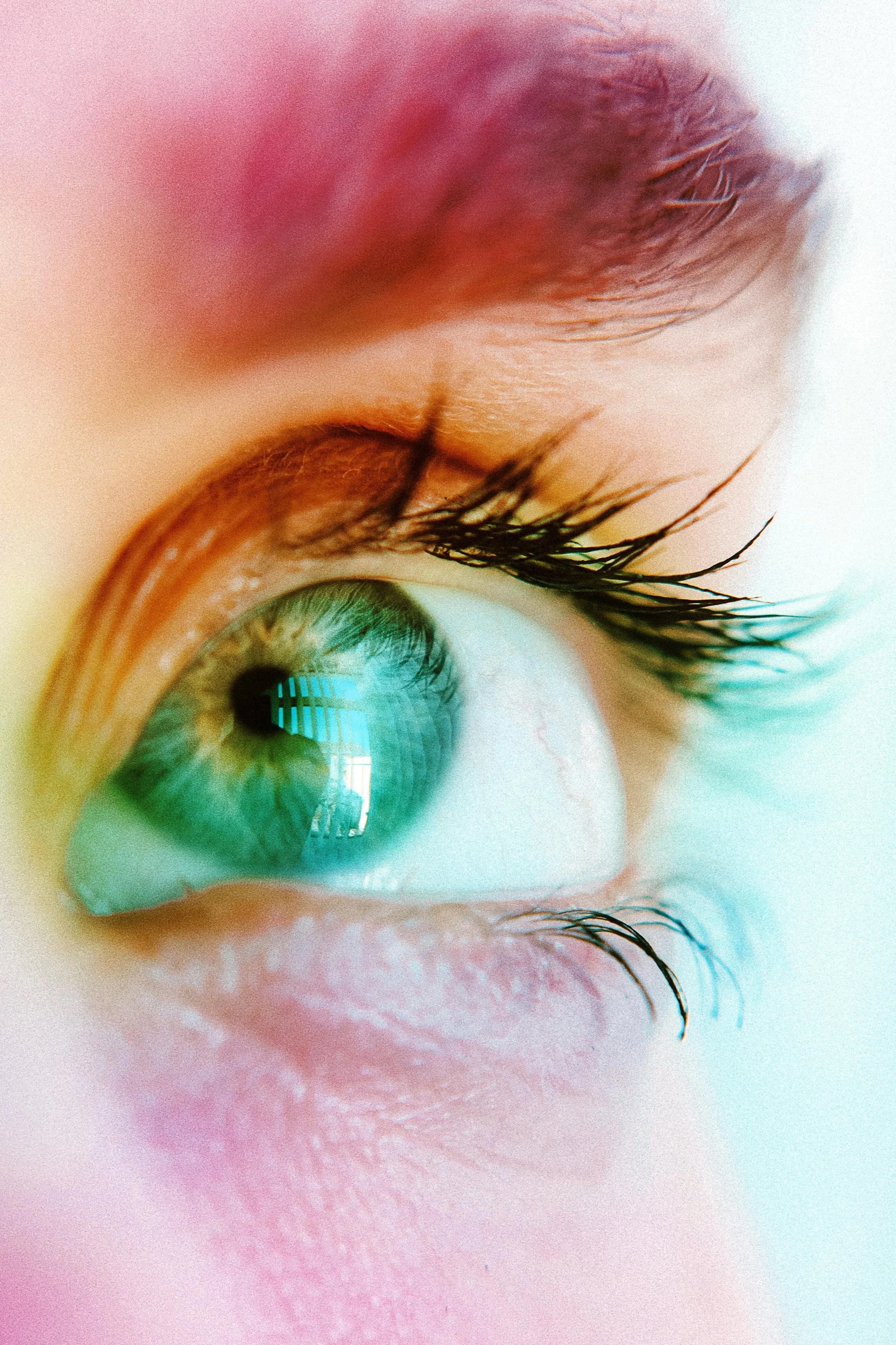 Close-up of a person's eye with green iris and long eyelashes, showing reflections on the cornea and colorful makeup around the eye.