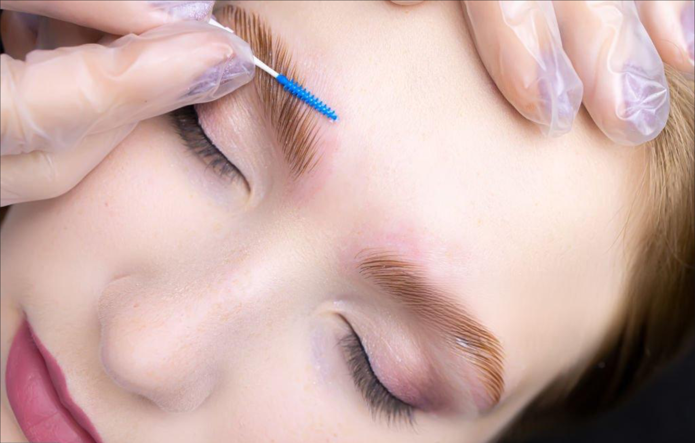 Close-up of a person receiving brow lamination, with an artist using a tool near the eye while wearing gloves.