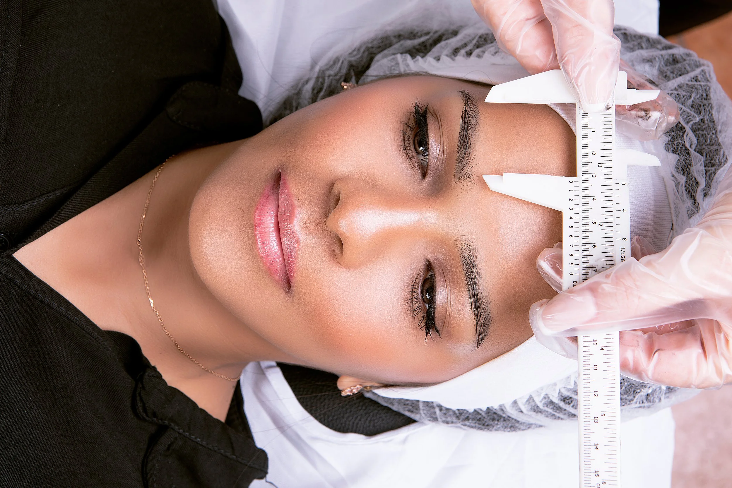 A woman lying down while a gloved person measures her forehead with a ruler.