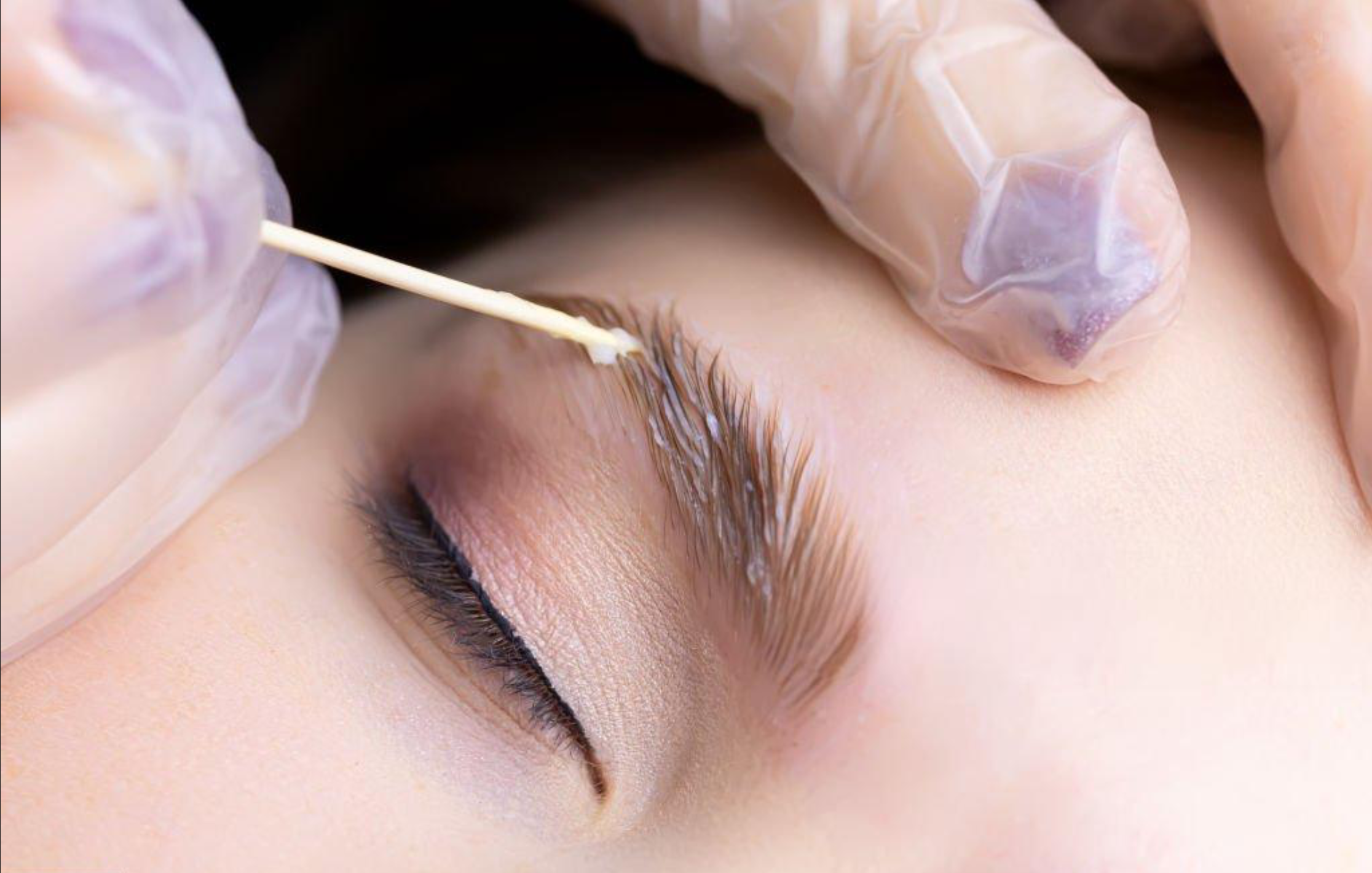 Close-up of a person's eye with someone wearing gloves performing eyebrow lamination.