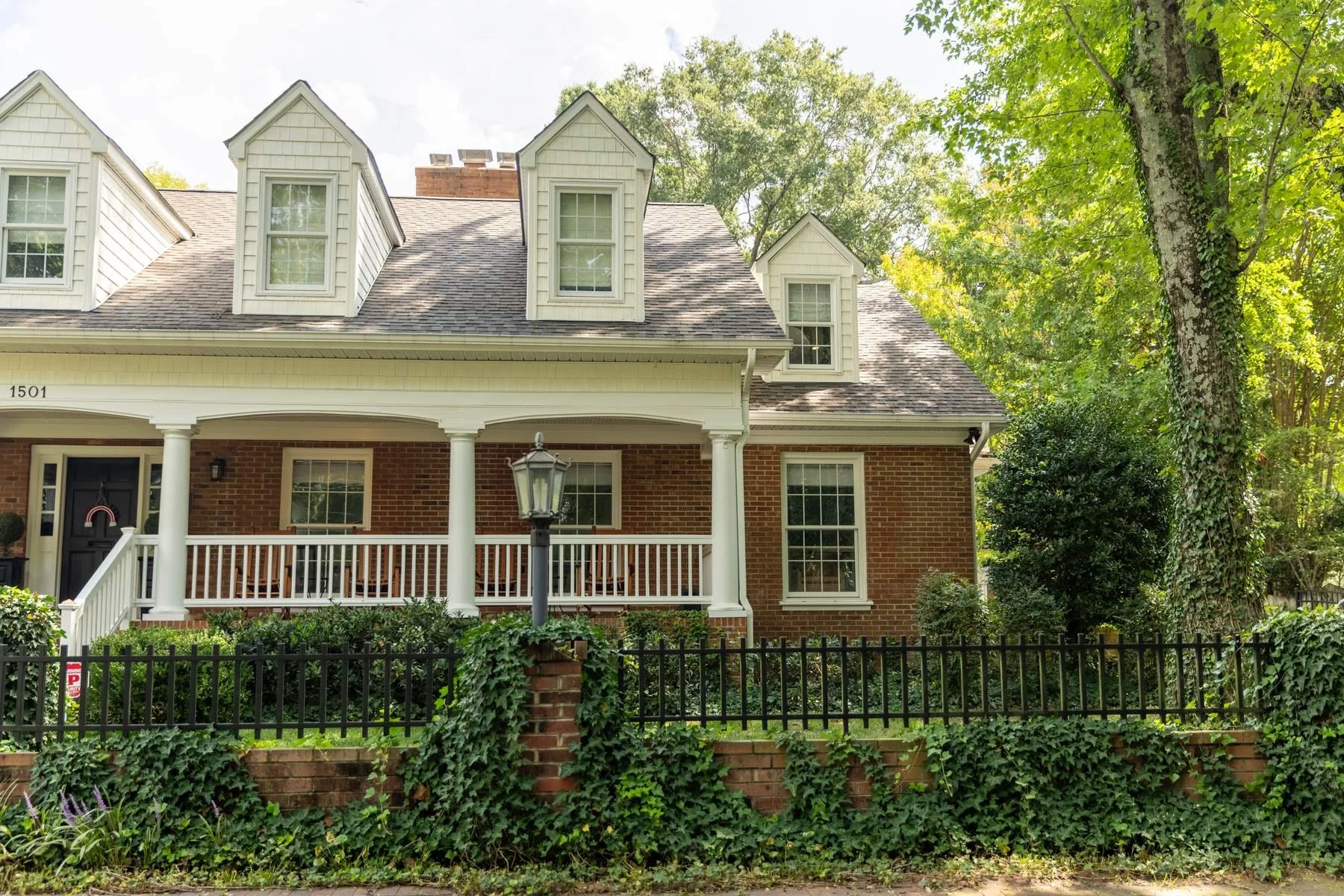 Front exterior of a white dormered home with a covered front porch and brick foundation, a whole-home renovation in Charlotte, NC