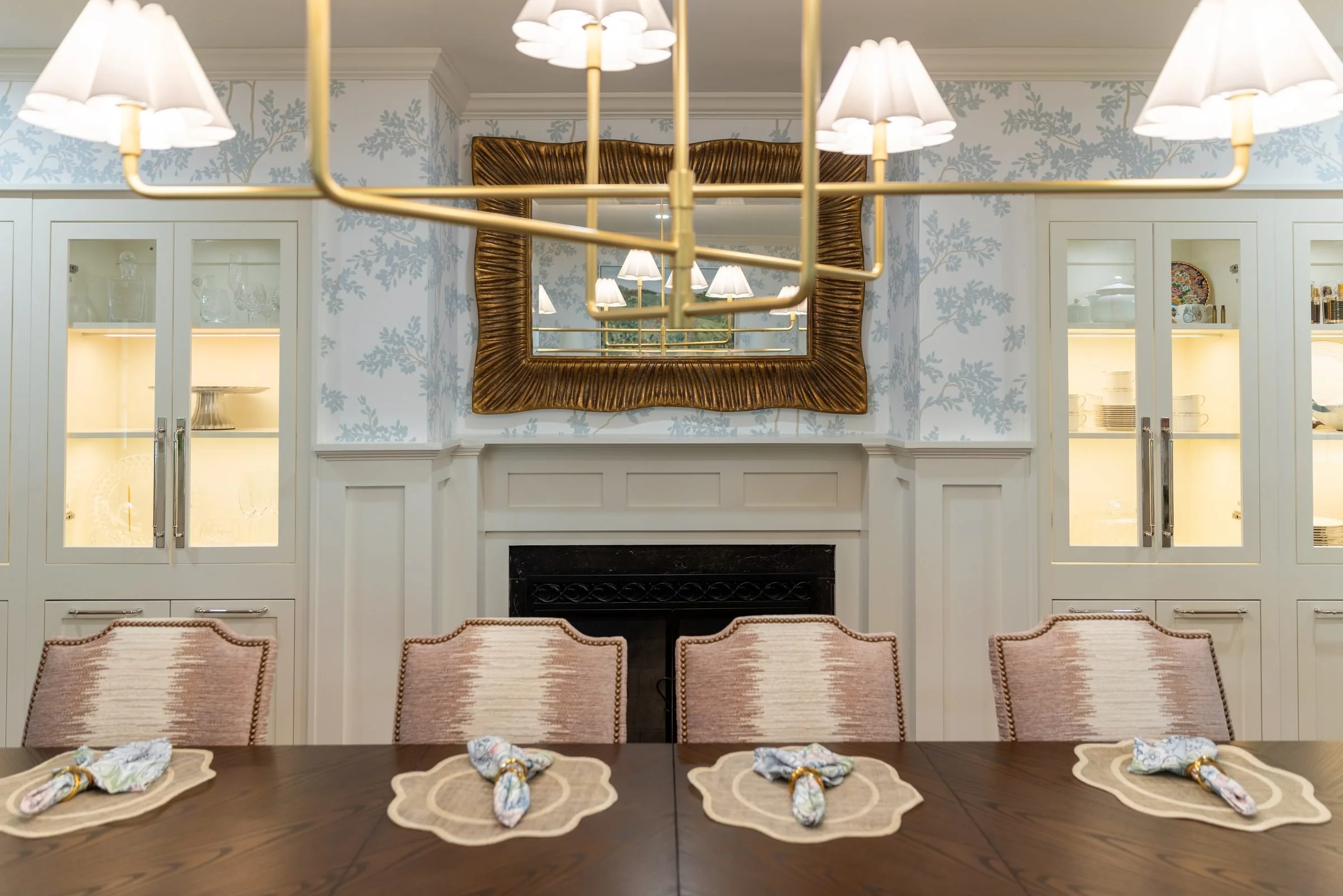 Dining room fireplace wall with gilded mirror, flanking glass-front cabinets, and a brass chandelier in a Charlotte, NC home