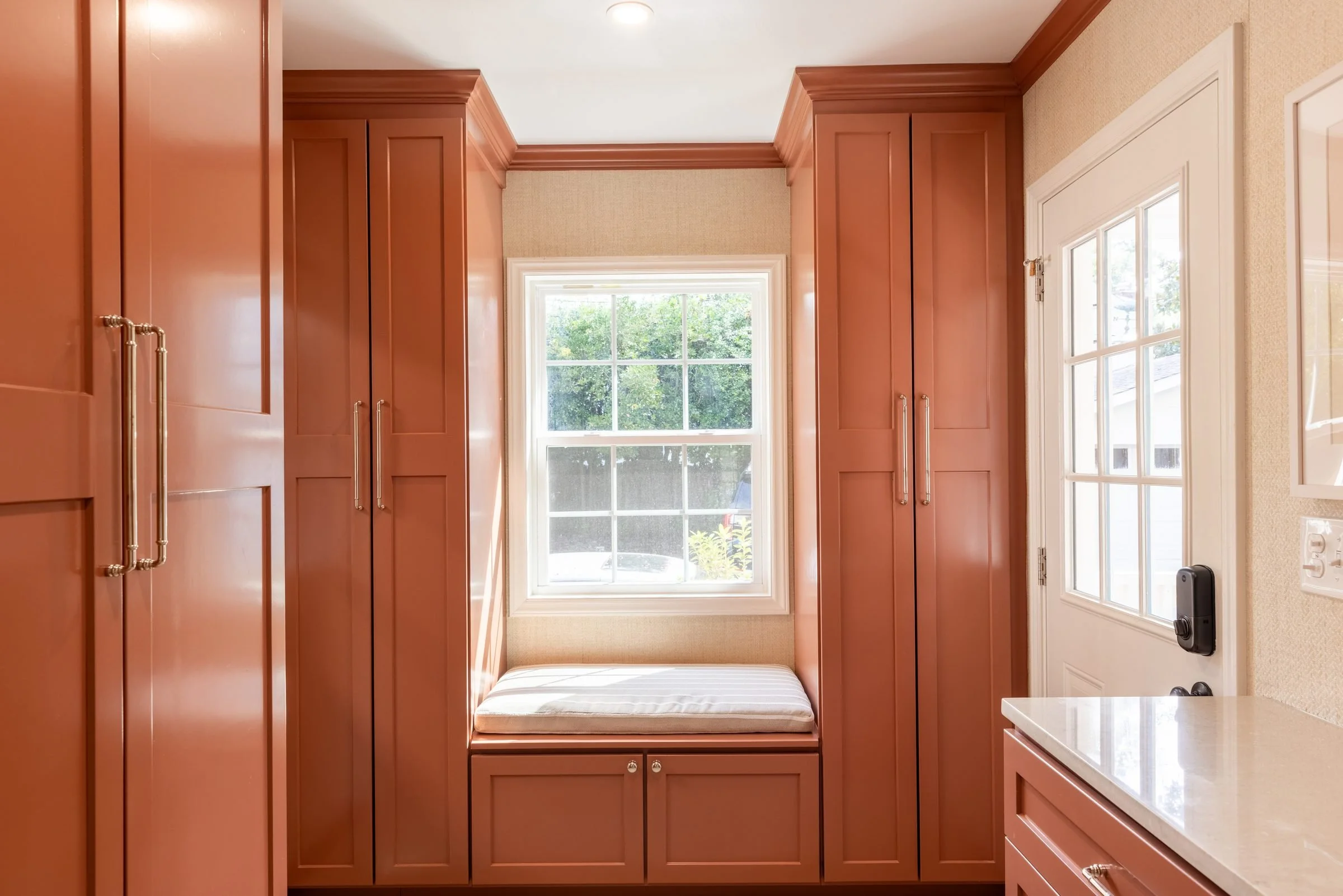 Glossy coral mudroom built-ins with tall storage cabinets and a window seat from a Charlotte, NC whole-home renovation