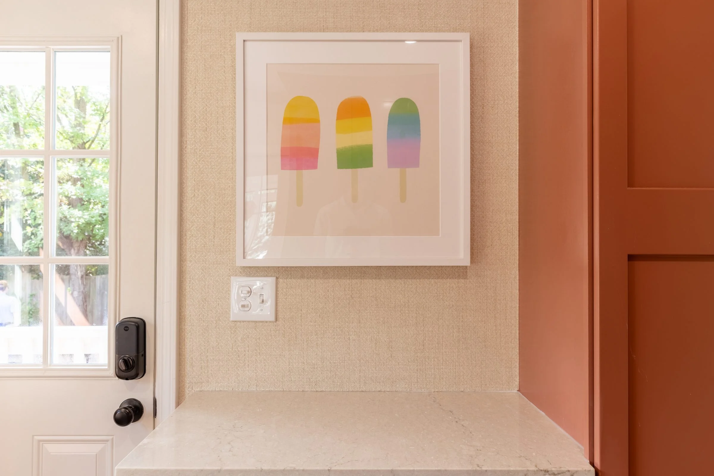 Coral mudroom cabinetry beside a white entry door with colorful framed art in a renovated Charlotte, NC home