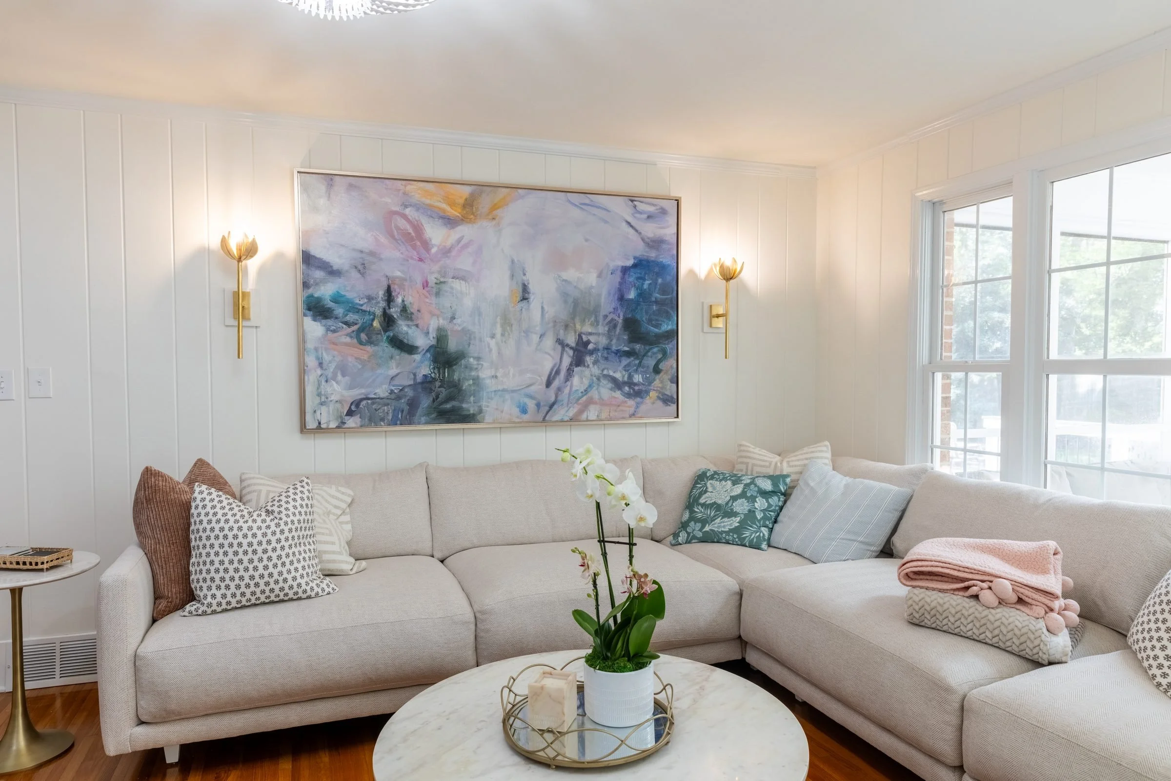Bright living room with white sectional, brass sconces, and abstract art in a Charlotte, NC whole-home renovation