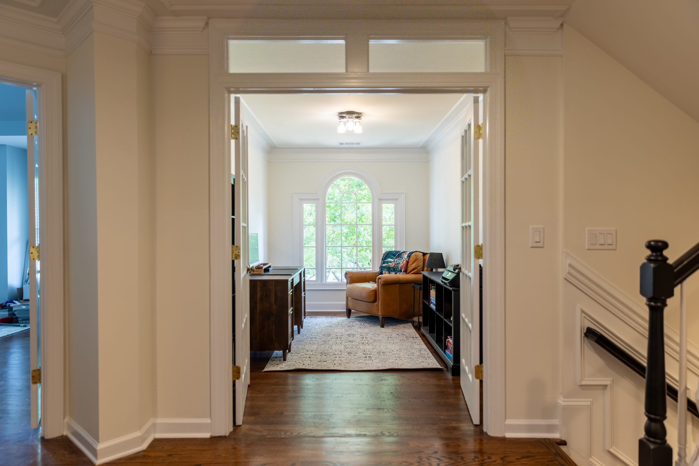 Hallway with dark-stained stair rail leading to a study with an arched window in a renovated Charlotte, NC home