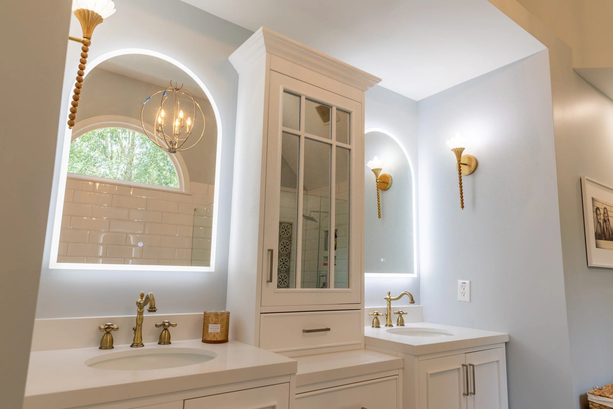 Arched backlit vanity mirror and white cabinetry with brass fixtures in a renovated Charlotte, NC primary bath