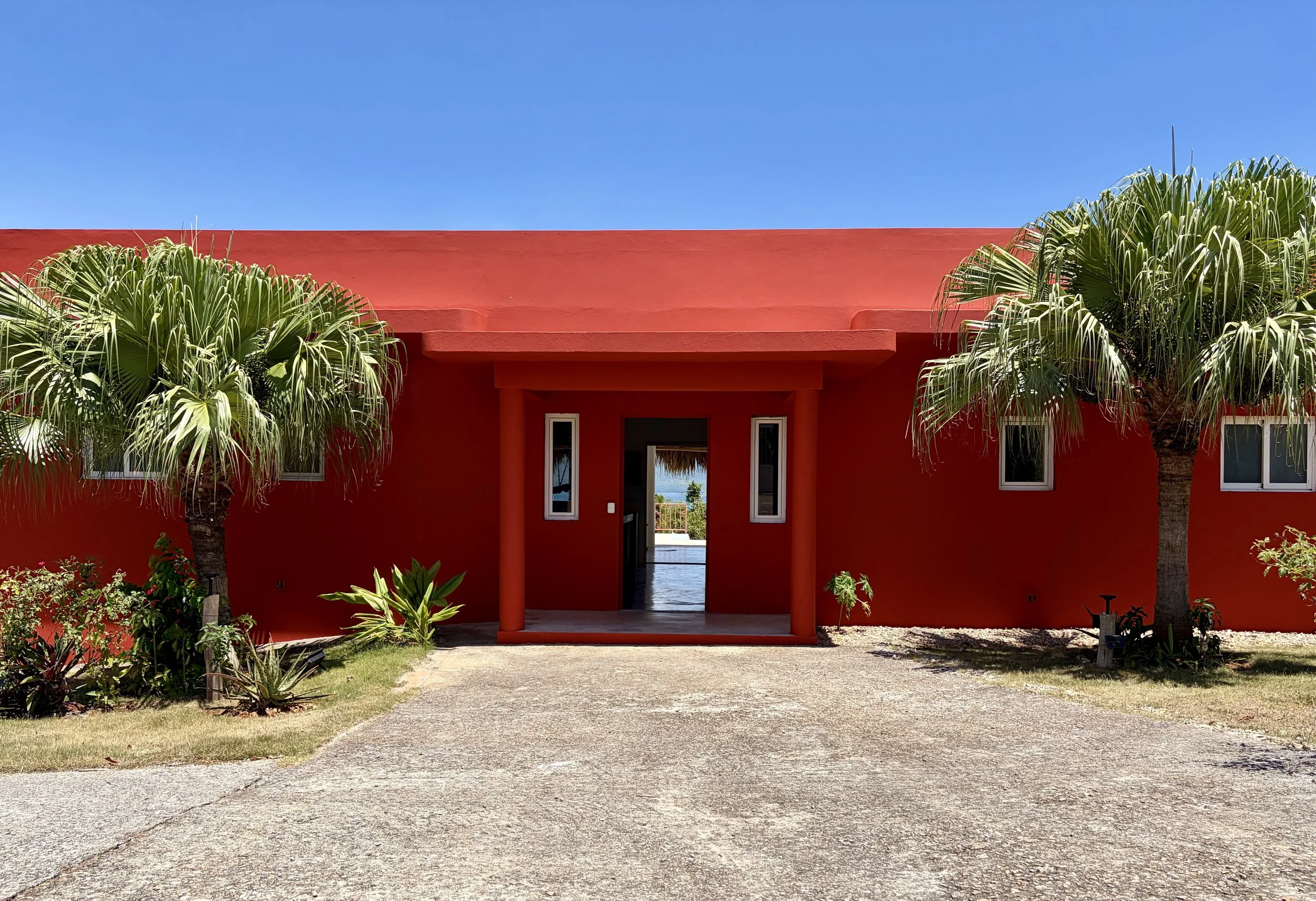 Front view of Villa Caribana, a one-story house surrounded by a tropical garden, with a glimpse of the sea visible through the entrance.