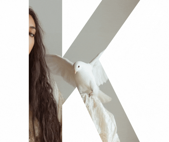 A woman with long curly hair holding a white dove on her finger indoors. At YA SOKO