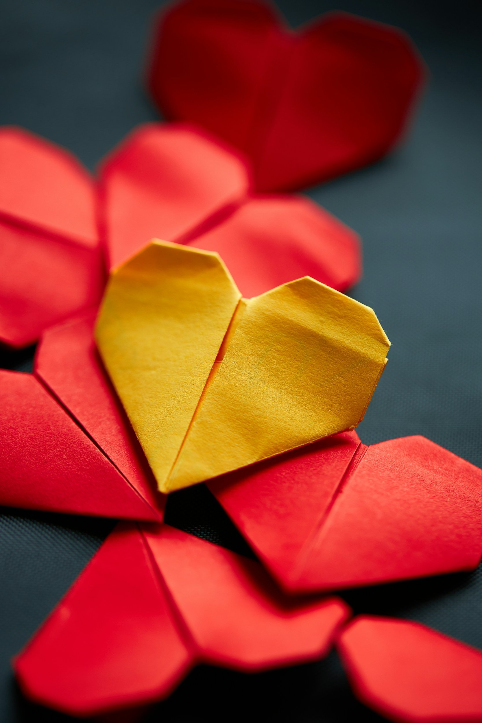 Close-up of origami hearts in yellow, red, and orange colors on a dark surface.