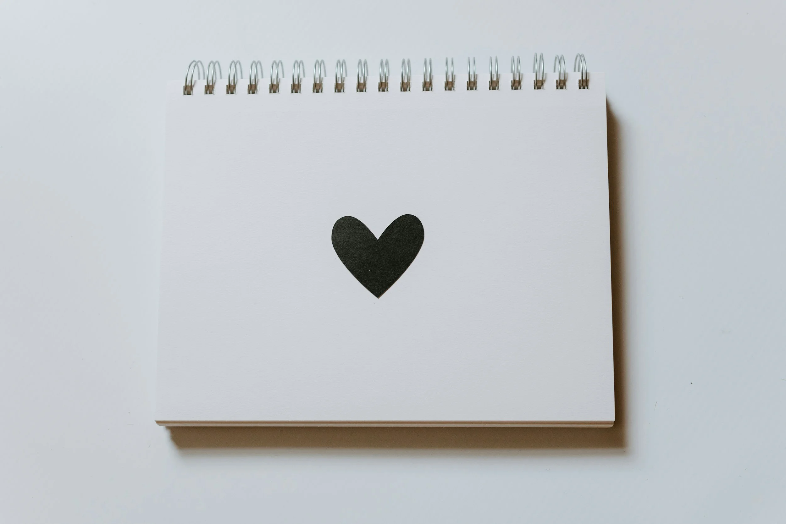 A spiral-bound desk calendar with a black heart on the page, placed on a white surface.
