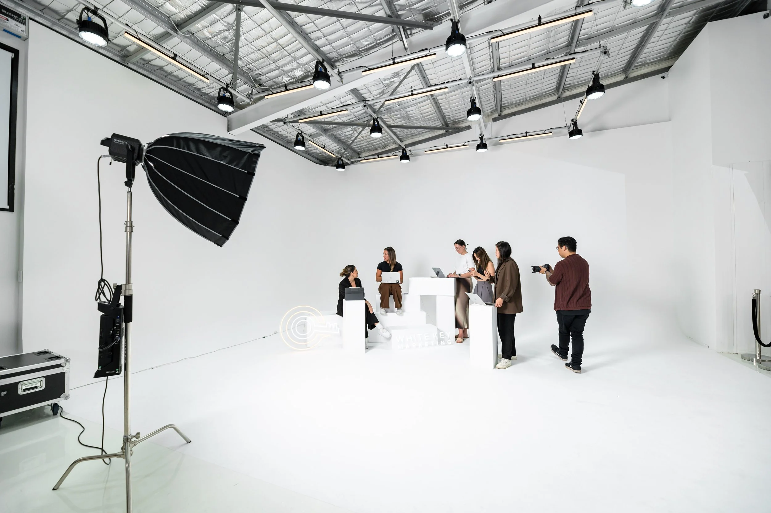 A photo of a photography studio with several people working, camera and lights set up, and a white backdrop.