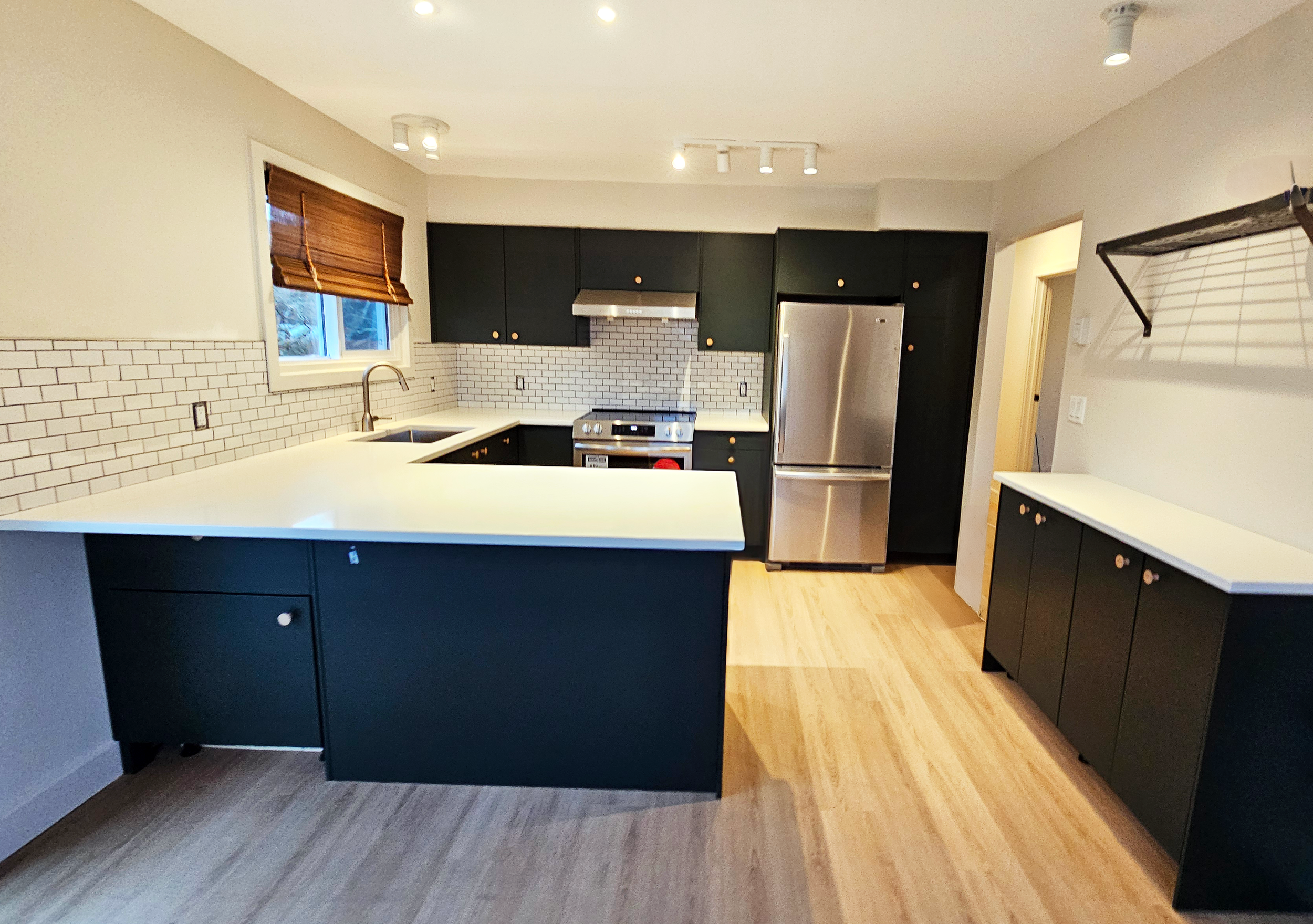 Modern kitchen with dark cabinets, stainless steel appliances, subway tile backsplash, and light wood flooring.