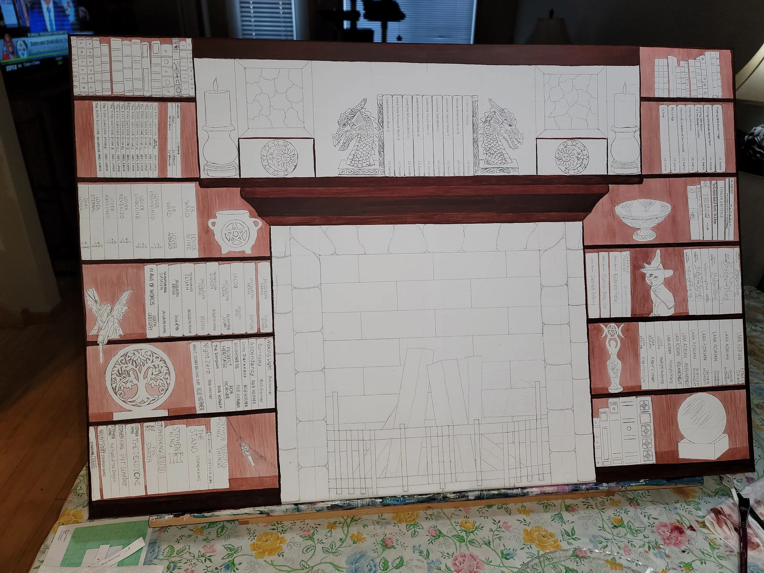 A large, partially painted board with detailed illustrations and text sections around the perimeter, including dragon heads, a witch, a tree, and various symbols and writings, with a fire place in the middle.