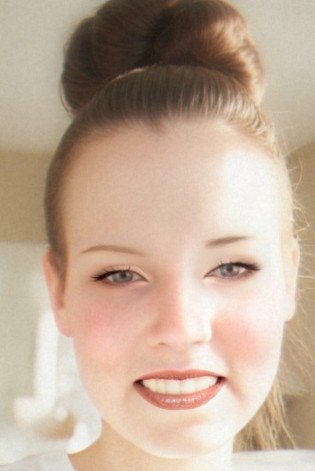 Close-up of the artist, Jennifer Sumner with light brown hair styled in a high bun, smiling slightly with lips parted, wearing makeup, and looking into the camera.