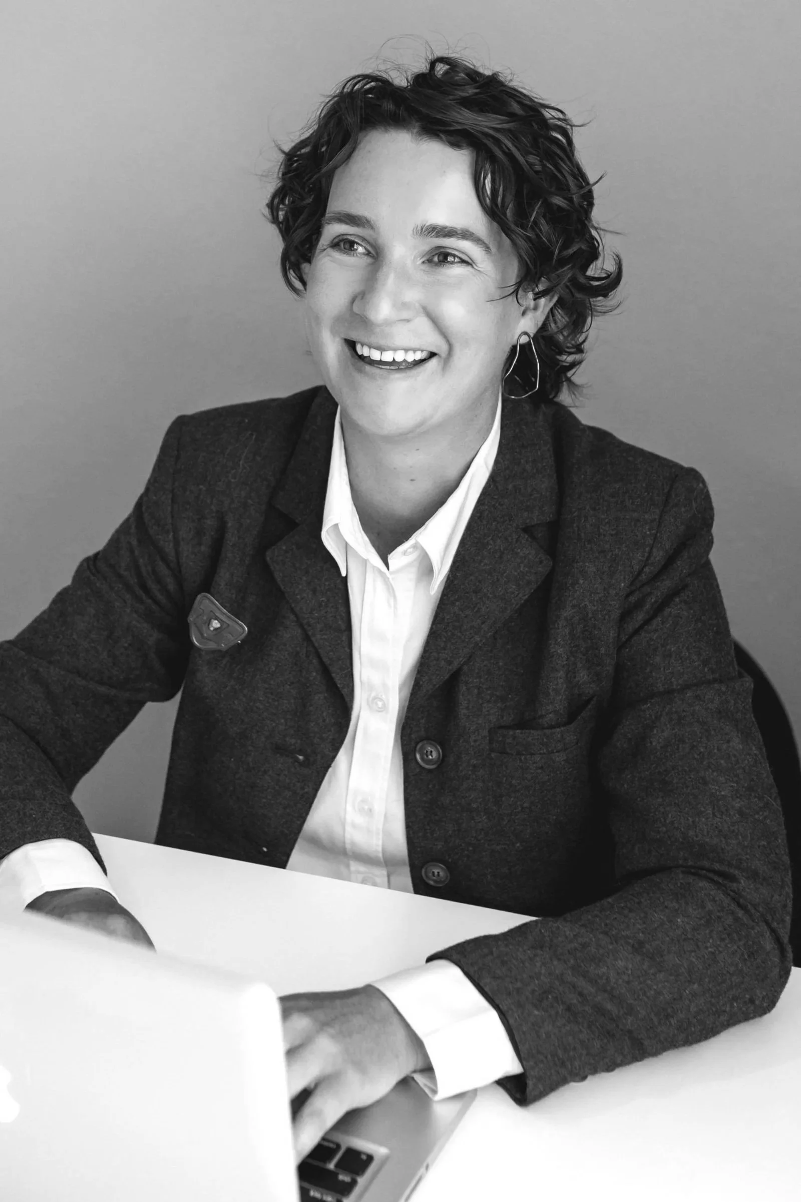 Person in a suit using a laptop, smiling, with curly hair and hoop earrings.