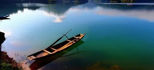 A wooden boat floating near the shore of a calm lake.