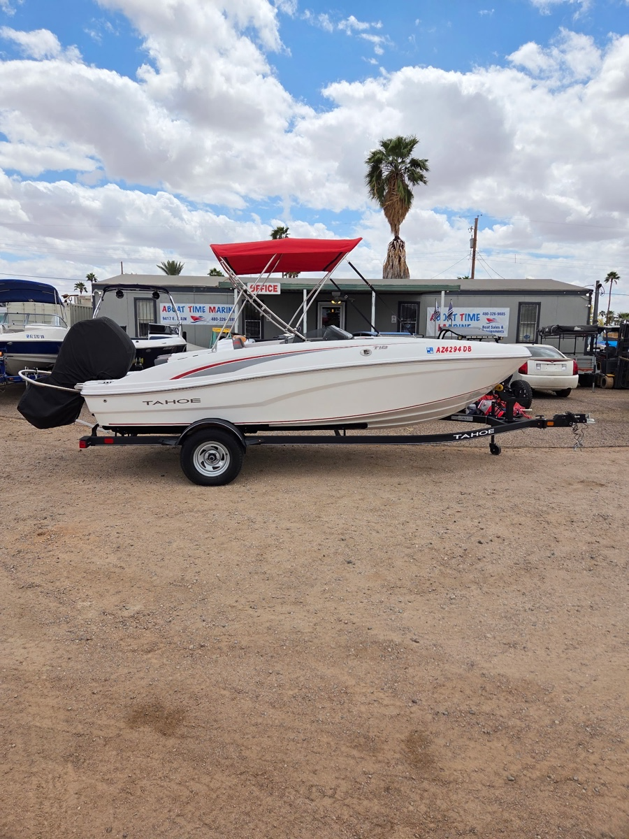 A white Tahoe speedboat on a trailer parked on a dirt lot with palm trees and a building in the background.