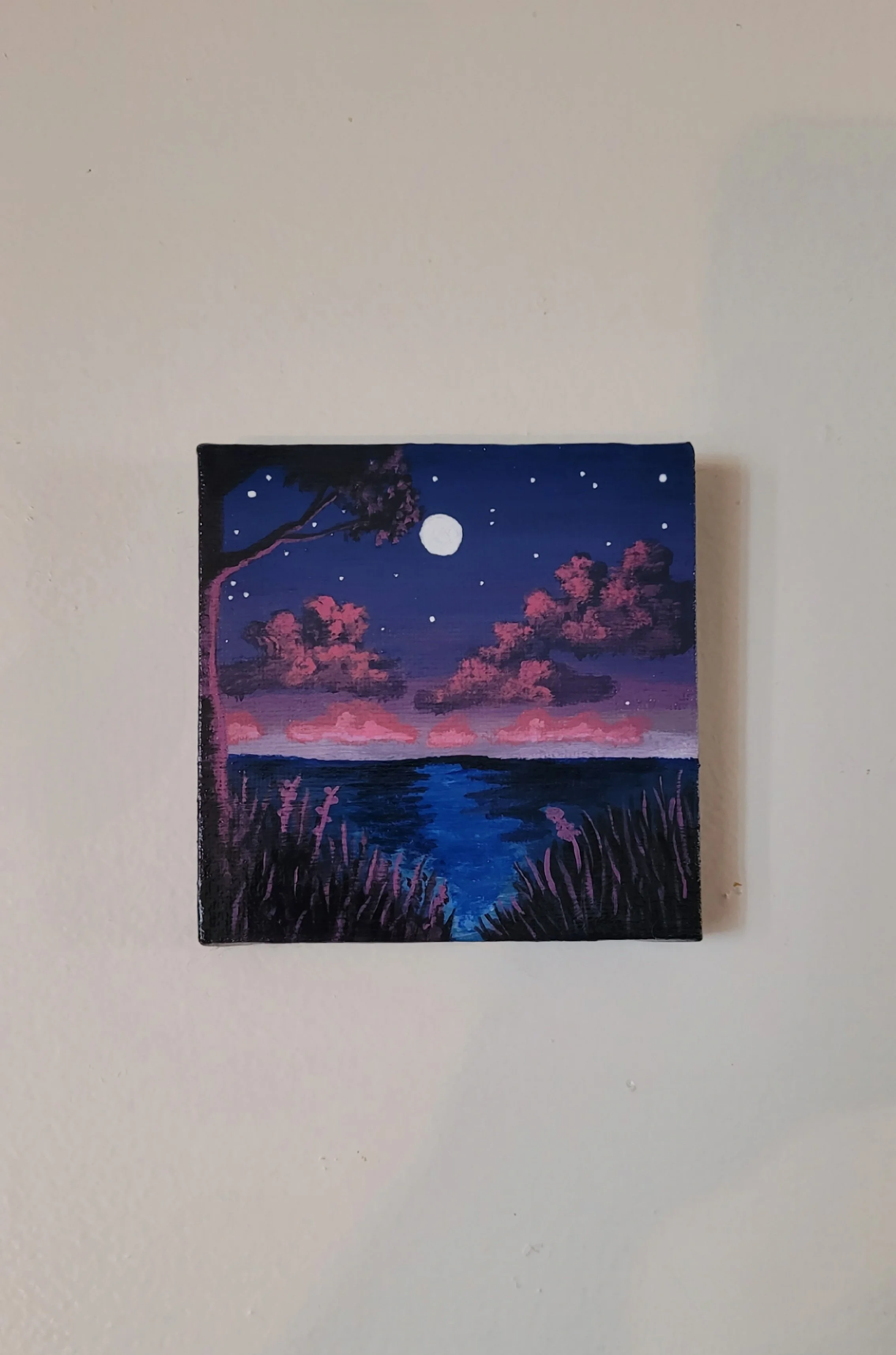 A painting of a night scene over a body of water, with pink clouds, a full moon, and a starry sky. There is a tree on the left and tall grass in the foreground.