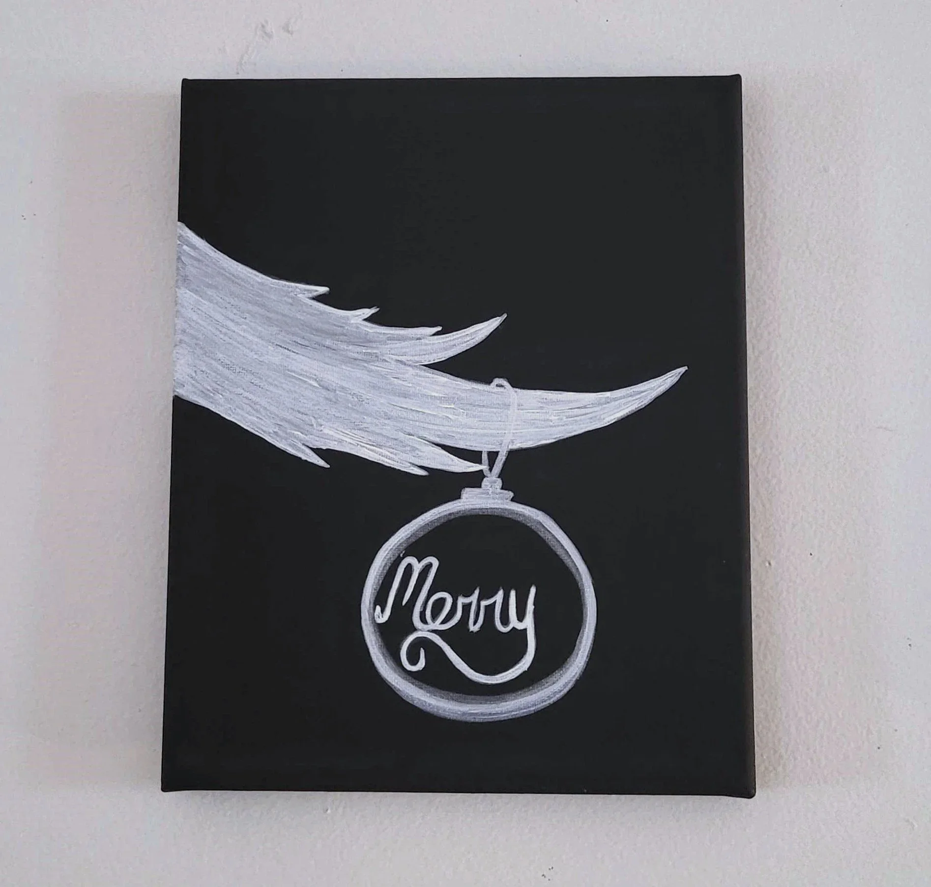 Black canvas with a white painted design of a hand holding a ring that has the word 'Merry' inside, resembling a holiday ornament.