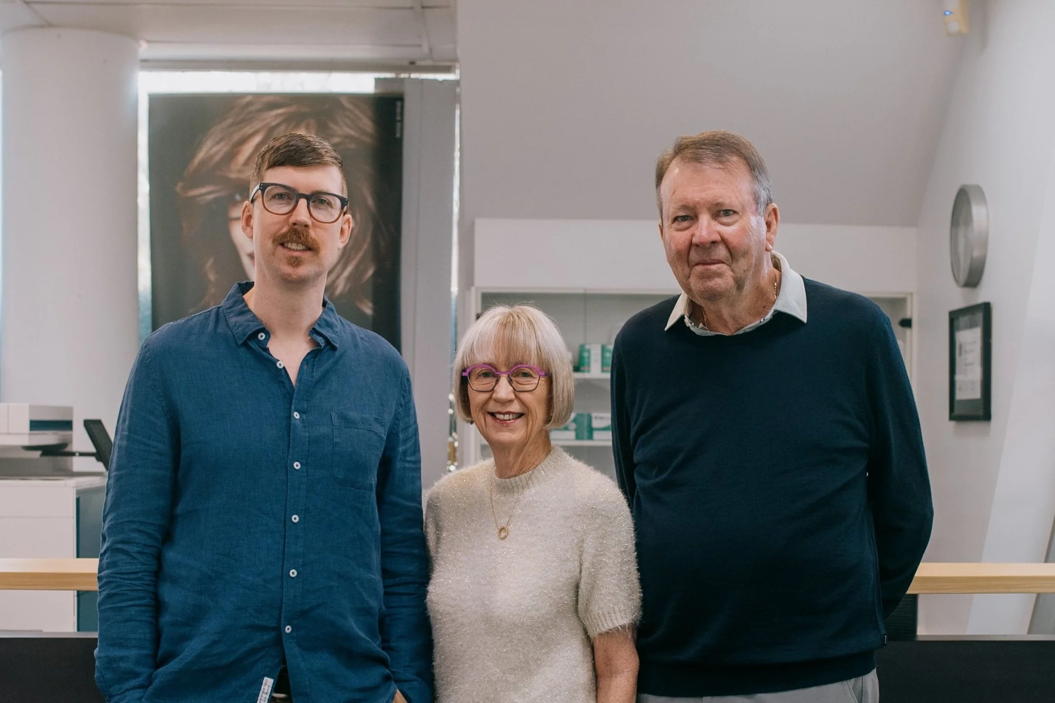 Three people standing together in an indoor setting, smiling at the camera.
