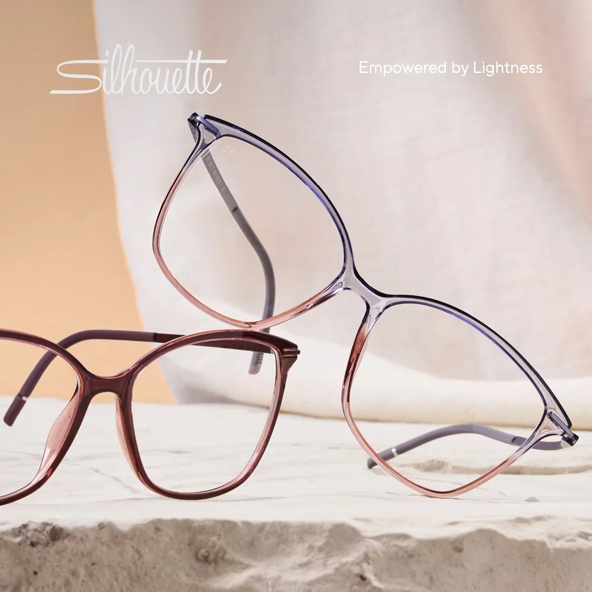 Two pairs of colorful eyeglasses, one pink and one purple, placed on a textured white surface with a blurred beige and light pink background.