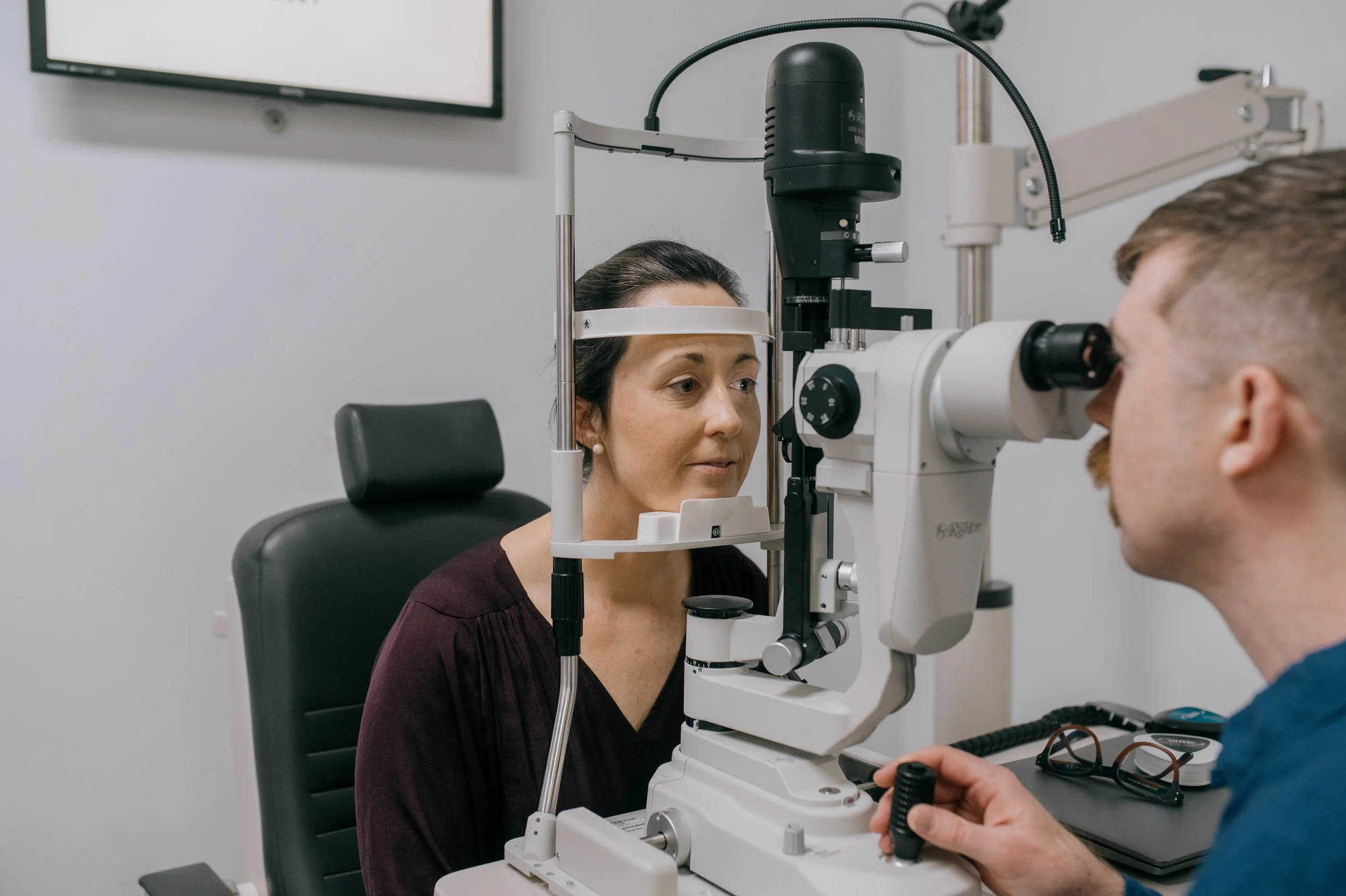 An optometrist examining a woman's eyes using a slit lamp microscope during an eye exam in an ophthalmology clinic.