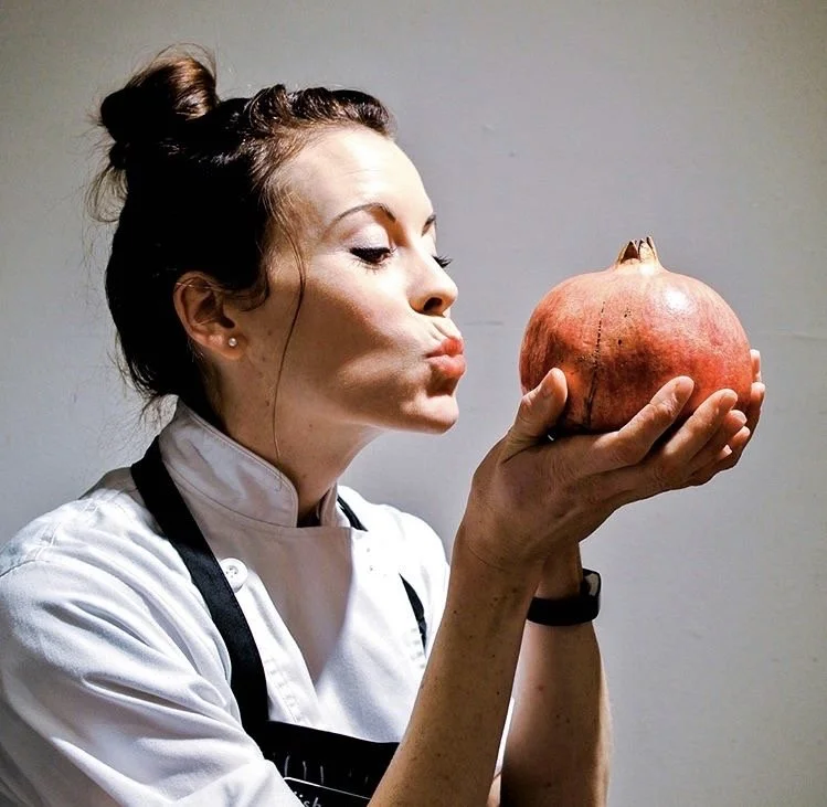 Chef holding a pomegranate and puckering lips as if to kiss it.