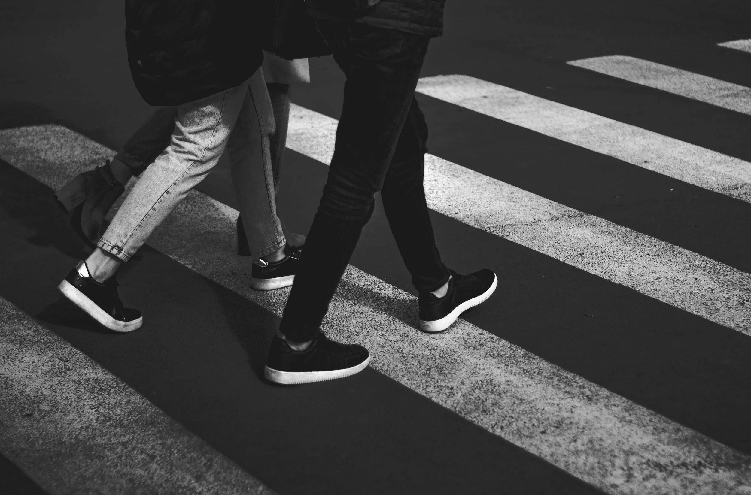 People crossing a street on a zebra crossing at night, shot in black and white from a low angle.