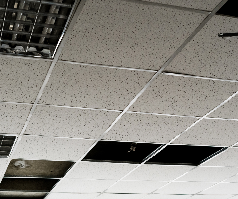 Ceiling tiles with some missing or damaged, exposing empty space and HVAC ductwork.