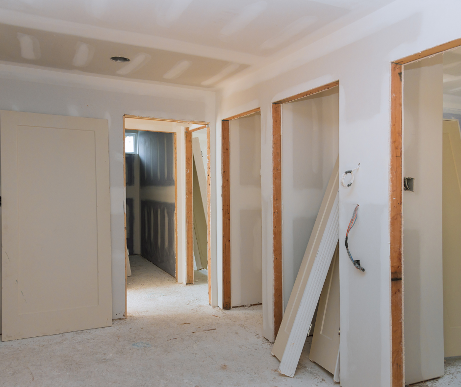 Interior view of a room under construction with door openings and exposed framing, drywall installation ongoing.