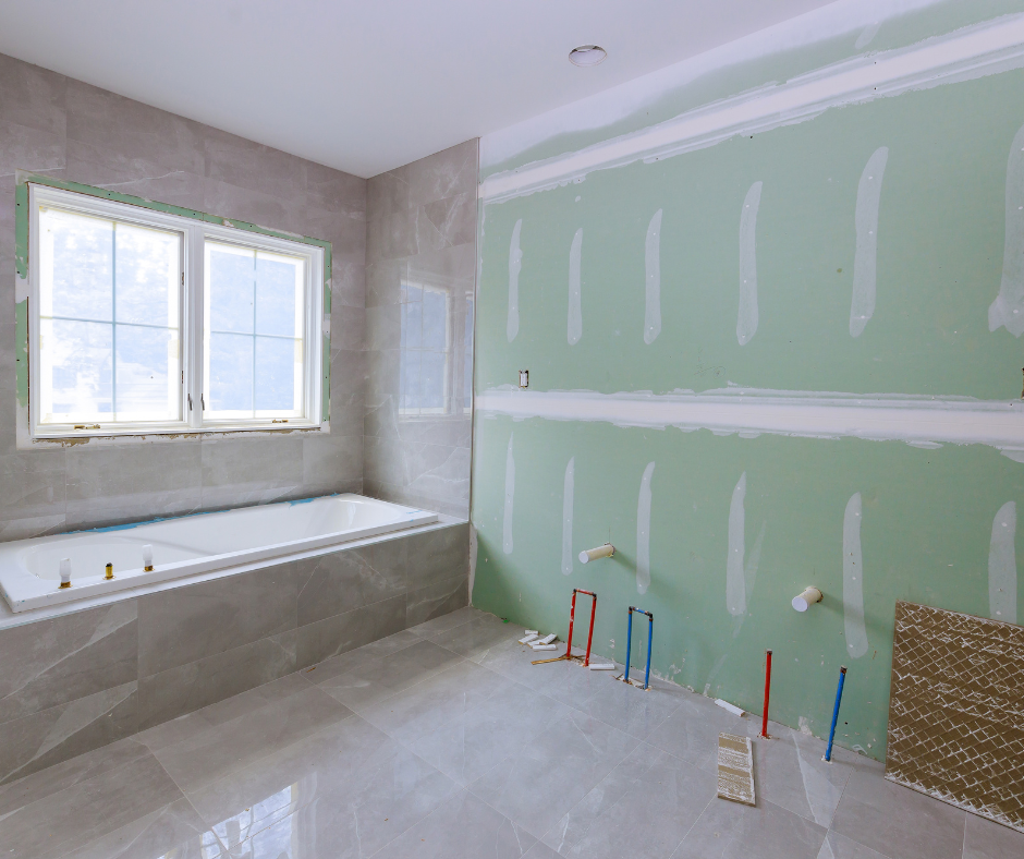 A bathroom under construction with a bathtub, a window, and partially finished green drywall with visible drywall joints and pipes.