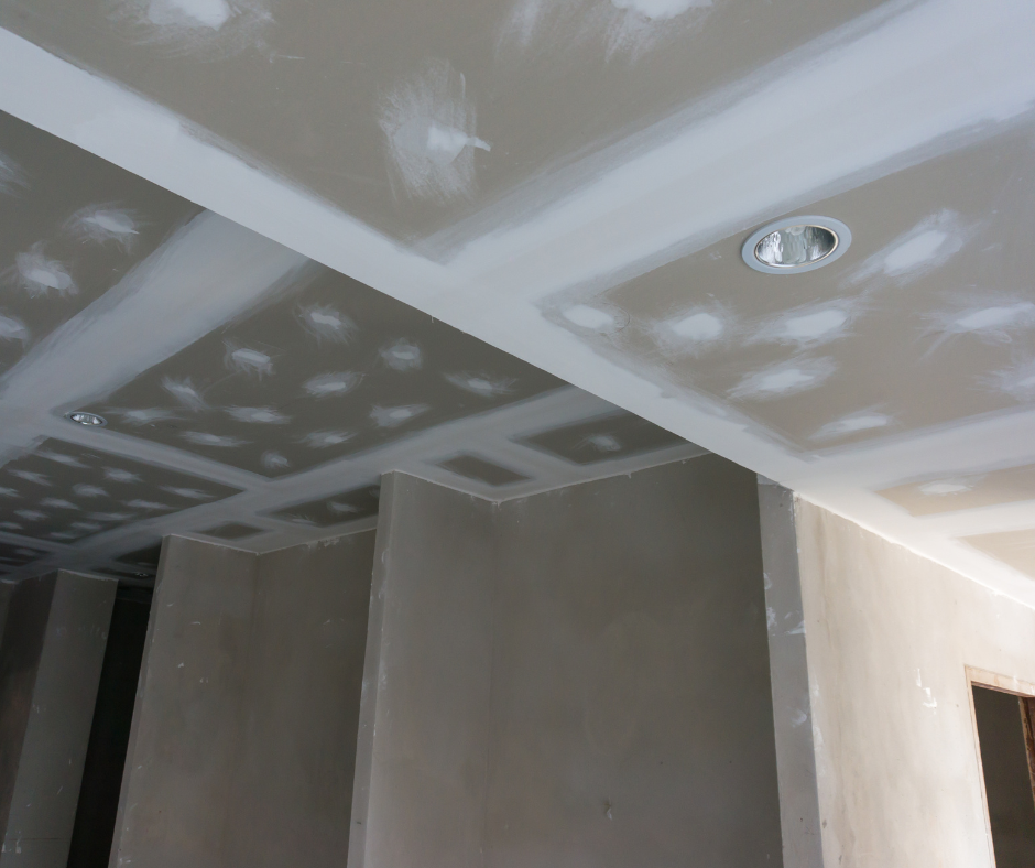 Ceiling with drywall in the process of being finished, showing joint compound and unfinished recessed lighting.