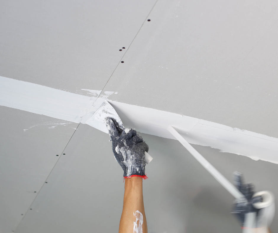 Person applying white joint compound to a drywall seam with a putty knife in a ceiling.