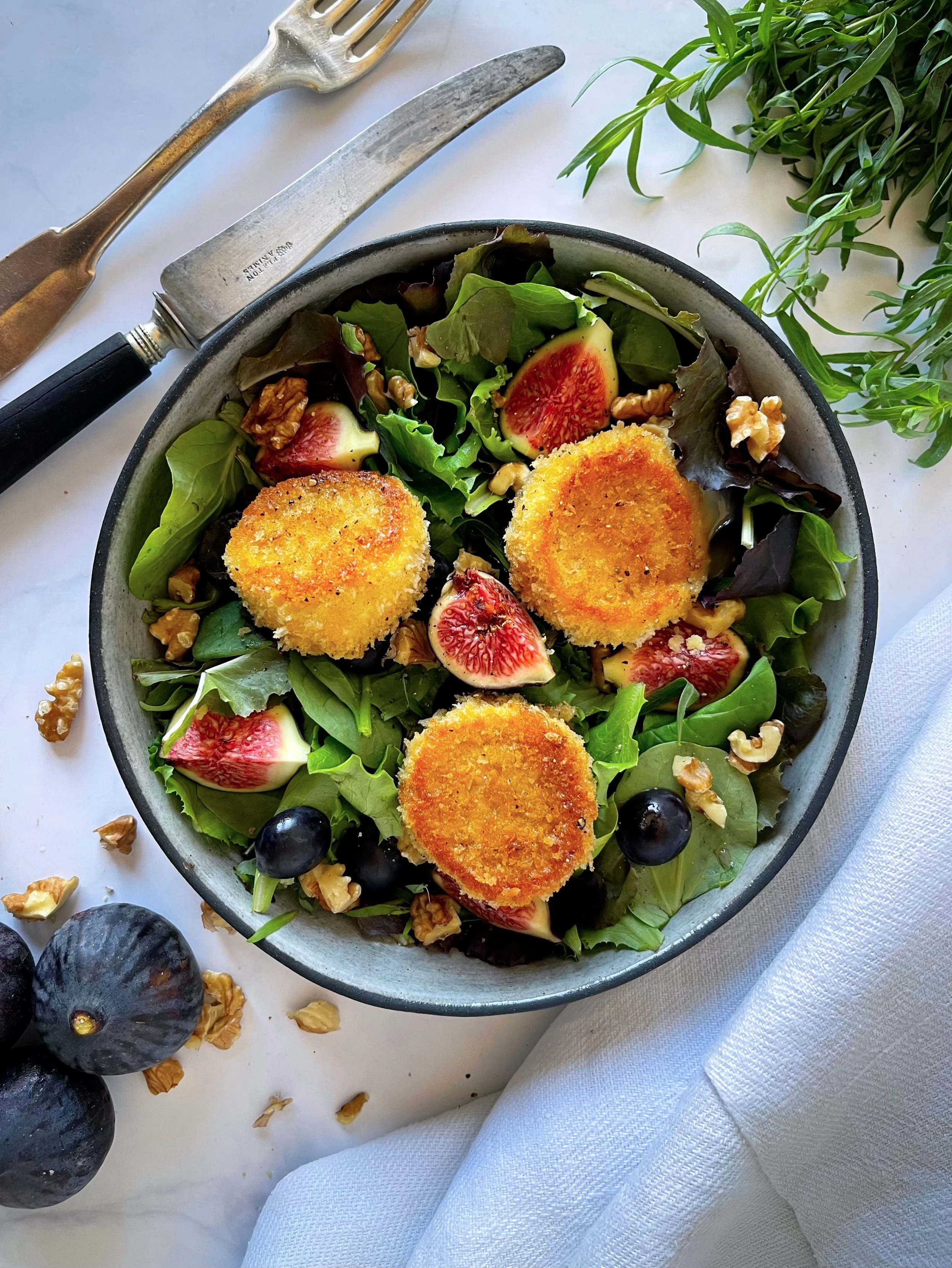 Assiette de salade de chèvre chaud : lit de mesclun, figues fraiches en quartier, raisins noir et cerneaux de noix. Petits fromage de chèvre panés sur le dessus