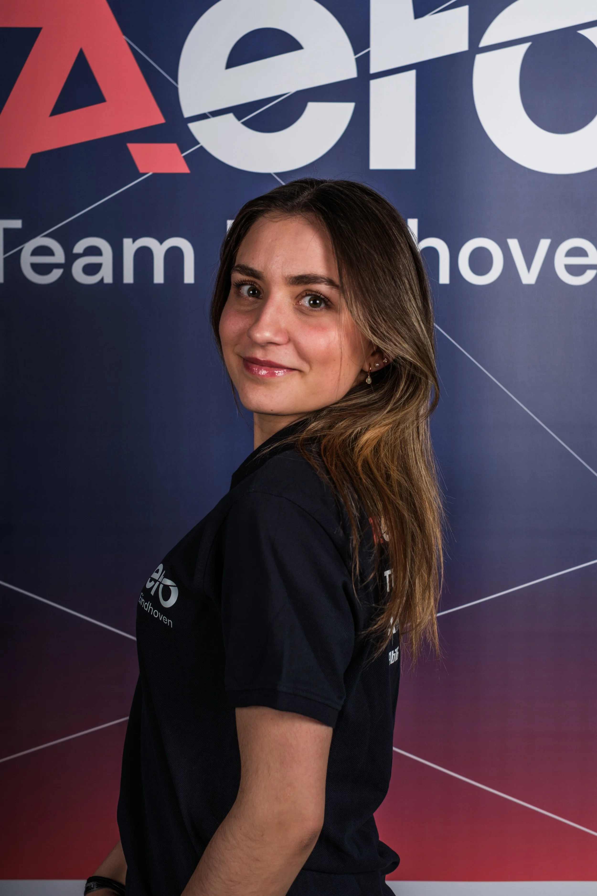 A young woman with long brown hair smiling in front of a dark blue backdrop with the words 'Team' and 'move' and a logo.