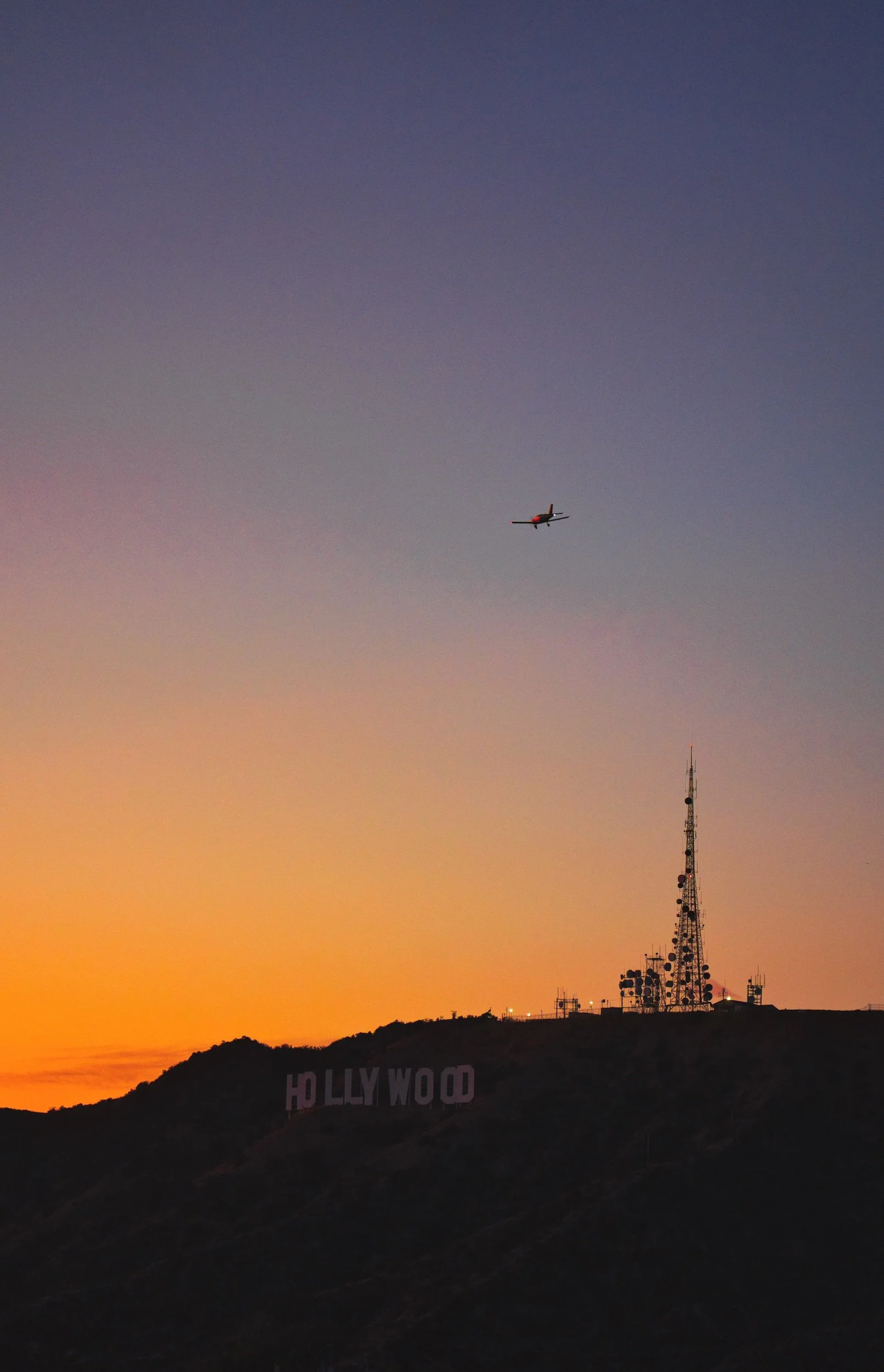 Sonnenuntergang bei den Hollywood Hills mit dem Hollywood-Schriftzug und einem Flugzeug am Himmel.