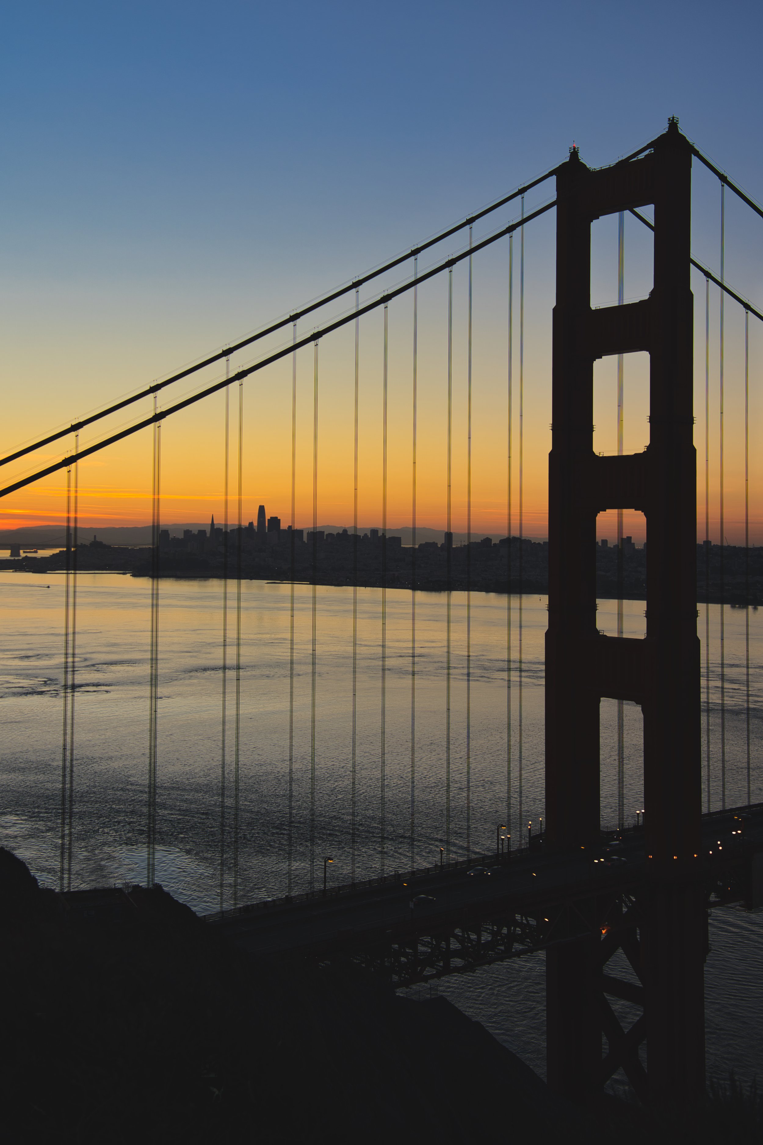 Sonnenuntergang über der Golden Gate Bridge in San Francisco, mit Blick auf die Skyline der Stadt im Hintergrund.