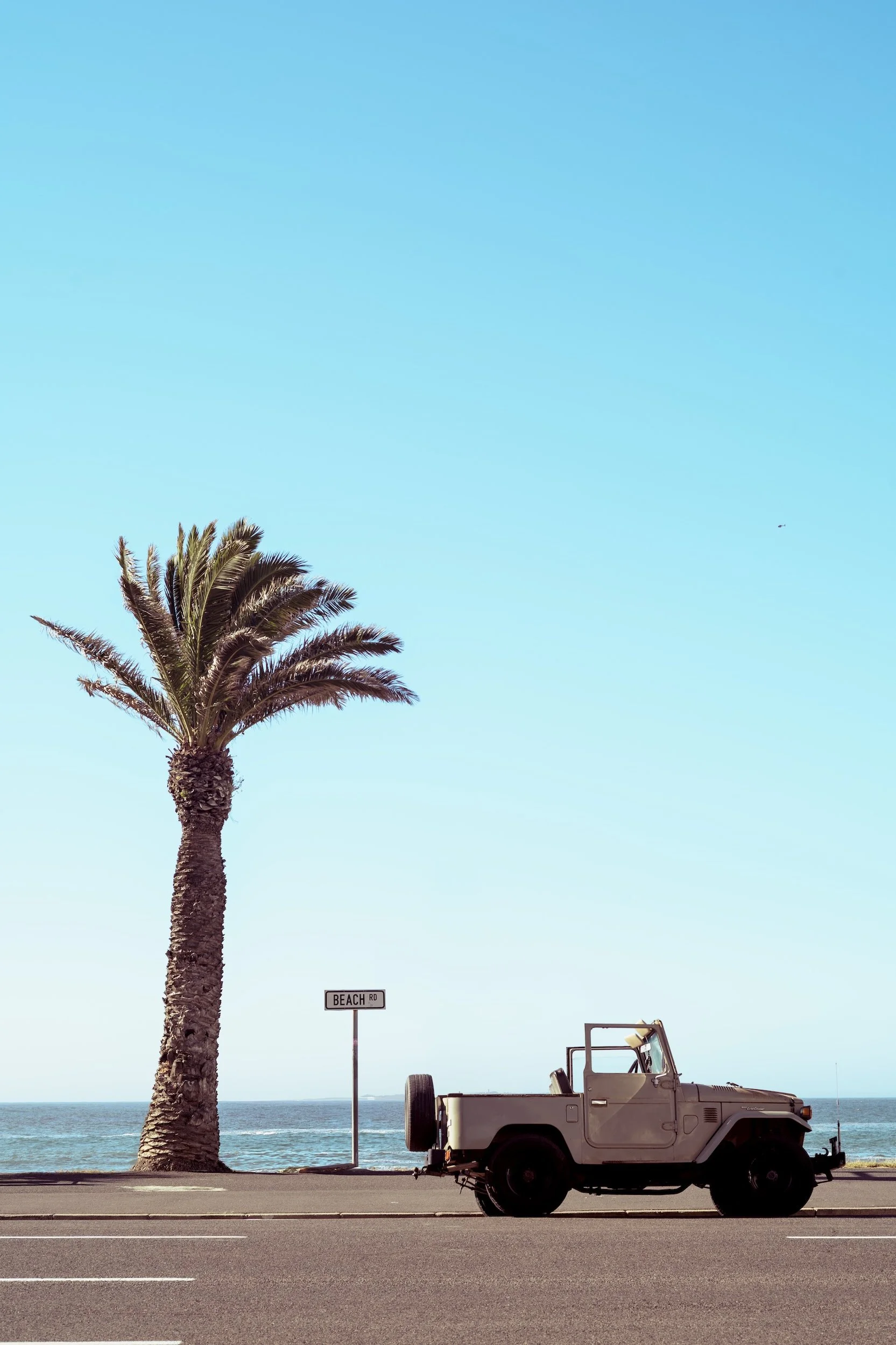 Vintage Toyota Land Cruiser parked on Beach Road next to a tall palm tree – Summer travel stills by Dario Caduff.