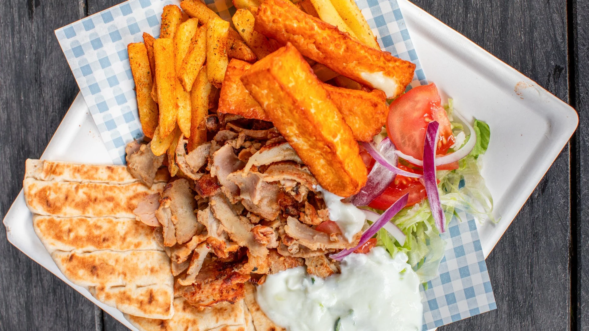 Plate of Lucky Gyros food including gyros meat, halloumi, fries, pita bread strips, side salad with tomatoes, lettuce, red onions, and tzatziki sauce