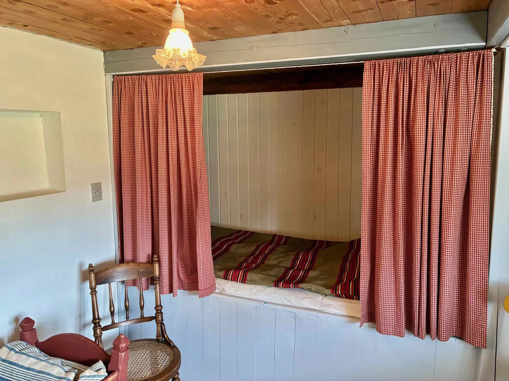 En seng med beige og røde striber, omgivet af røde tjekker gardiner.