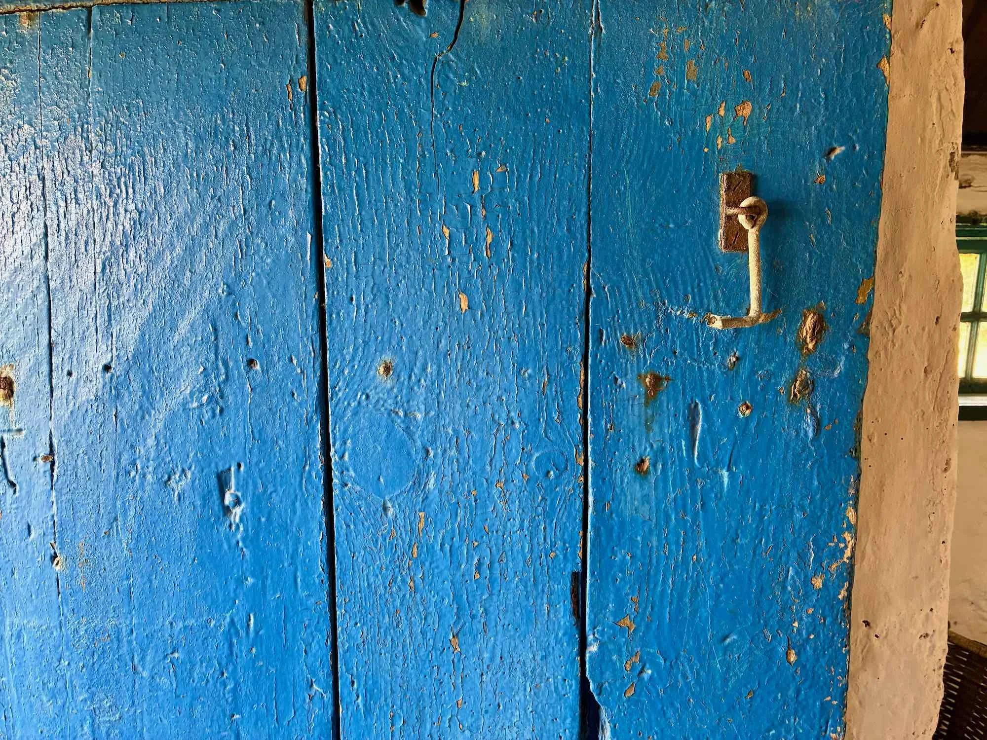 En gammel, blåmalet trædør med rustent håndtag.